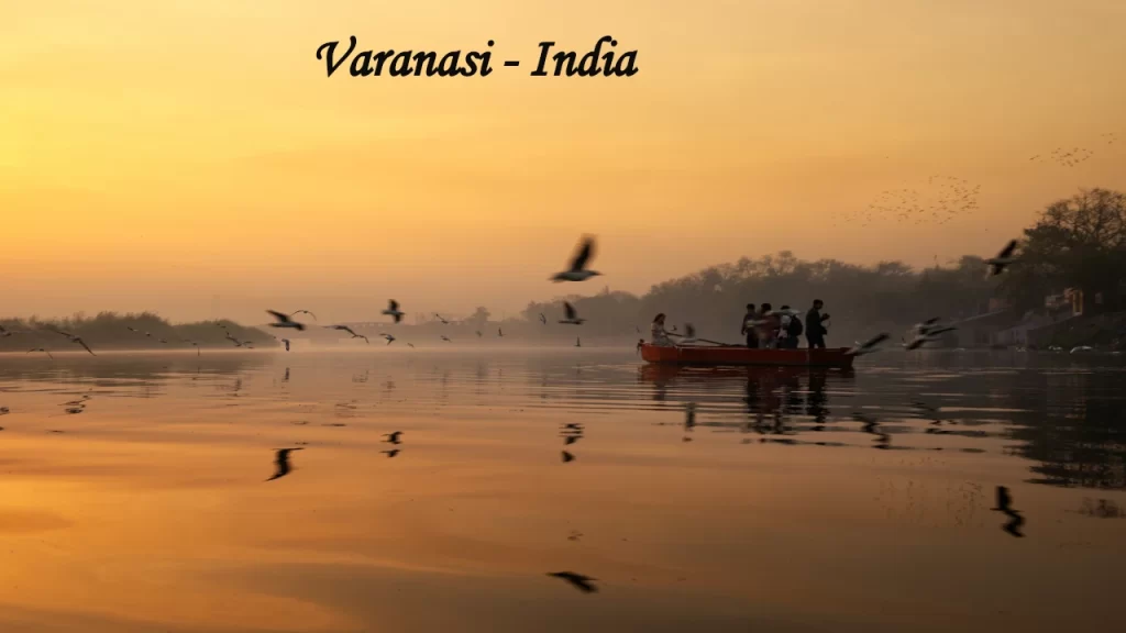 A serene sunrise over the Ganges River in Varanasi with a tourist boat and flying birds, capturing the spiritual essence of Indian travel.