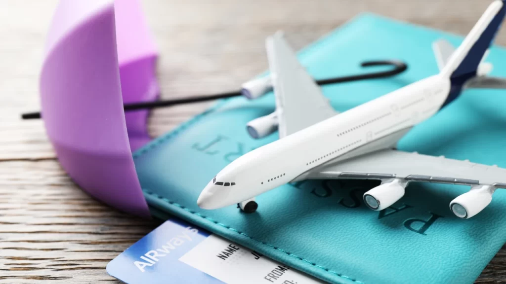 A toy airplane model, a boarding pass, and a passport in a turquoise cover on a wooden table, illustrating practical flight booking tips.