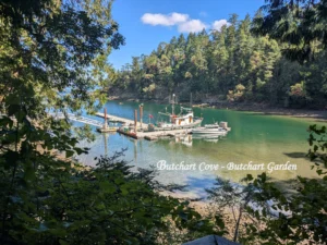 A scenic view through green trees of the boat dock at Butchart Garden Cove on Vancouver Island, British Columbia.