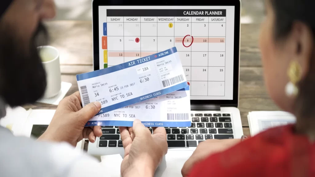 Couple planning travel on laptop calendar while holding business class tickets, applying smart flight booking tips.