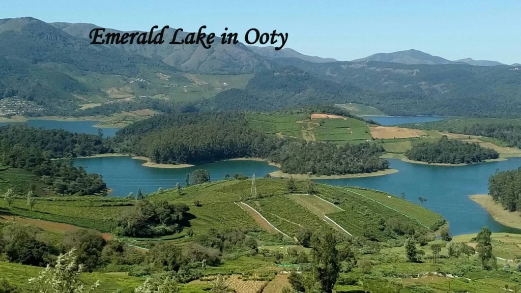 An aerial view of the serene turquoise Emerald Lake surrounded by green tea gardens and mountain slopes in Ooty.
