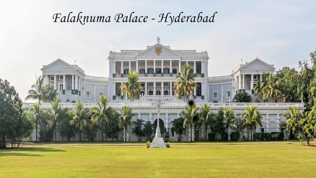 The grand white facade of Falaknuma Palace in Hyderabad, featuring Italian-style architecture, palm trees, and a spacious green lawn.