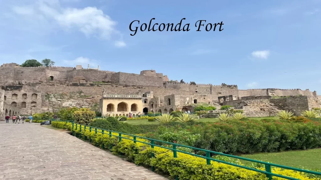 A scenic view of the historic ruins and stone walls of Golconda Fort in Hyderabad, featuring a beautifully landscaped garden in the foreground.