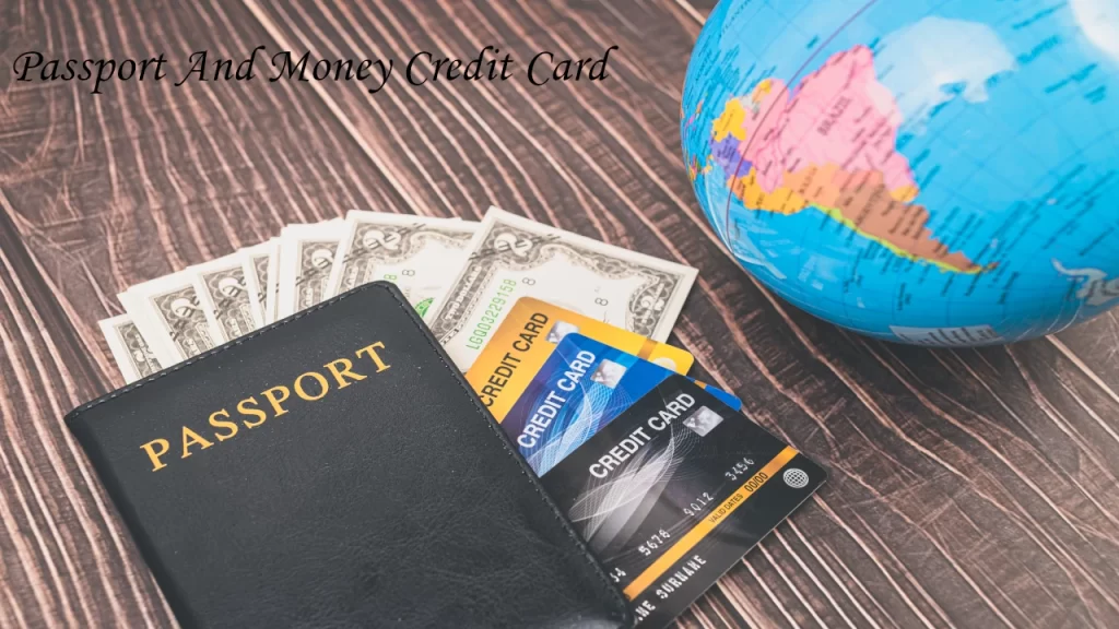 A black passport cover next to international credit cards, US currency notes, and a small desk globe on a wooden table.