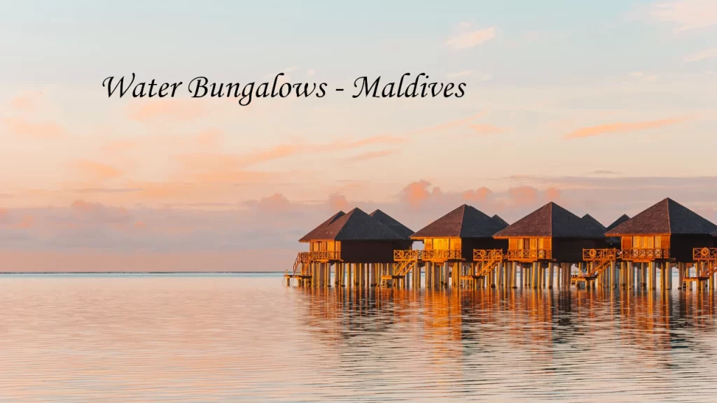 Row of wooden overwater bungalows glowing in warm sunset light reflected on the still lagoon in the Maldives — an exclusive destination wedding venue in Asia