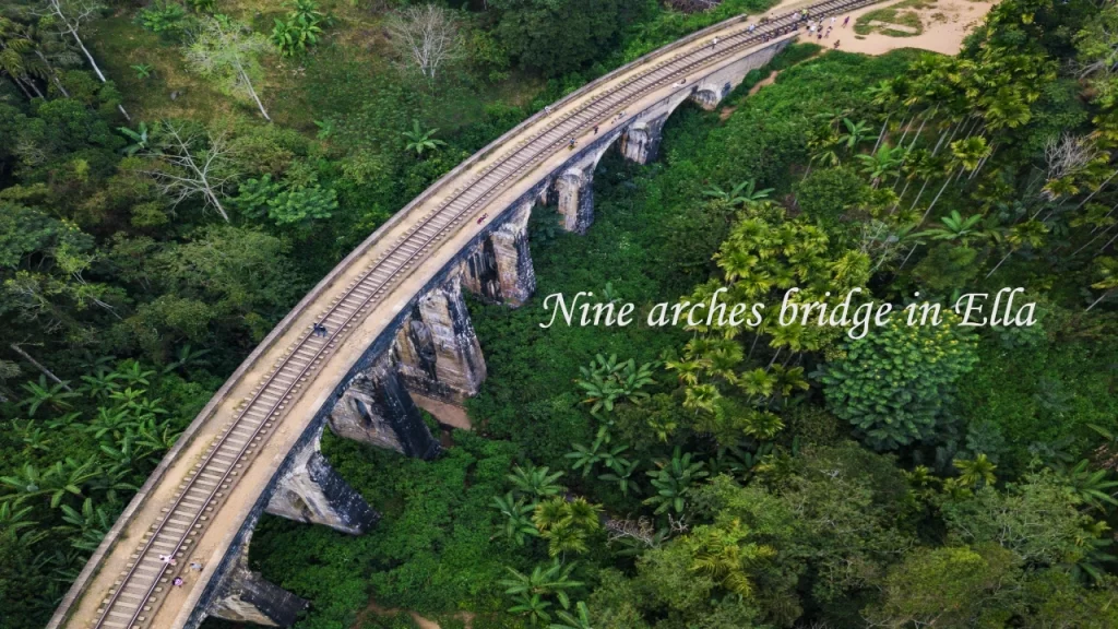 An overhead aerial view of the historic Nine Arches Bridge and train tracks enveloped by a lush tropical forest in Ella, one of the top hill stations in Sri Lanka.