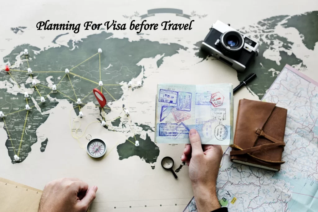 Flat lay overhead view of a person holding an open passport with stamps over a world map pinned with travel routes, surrounded by a vintage camera, compass, notebook, and a magnifying glass.