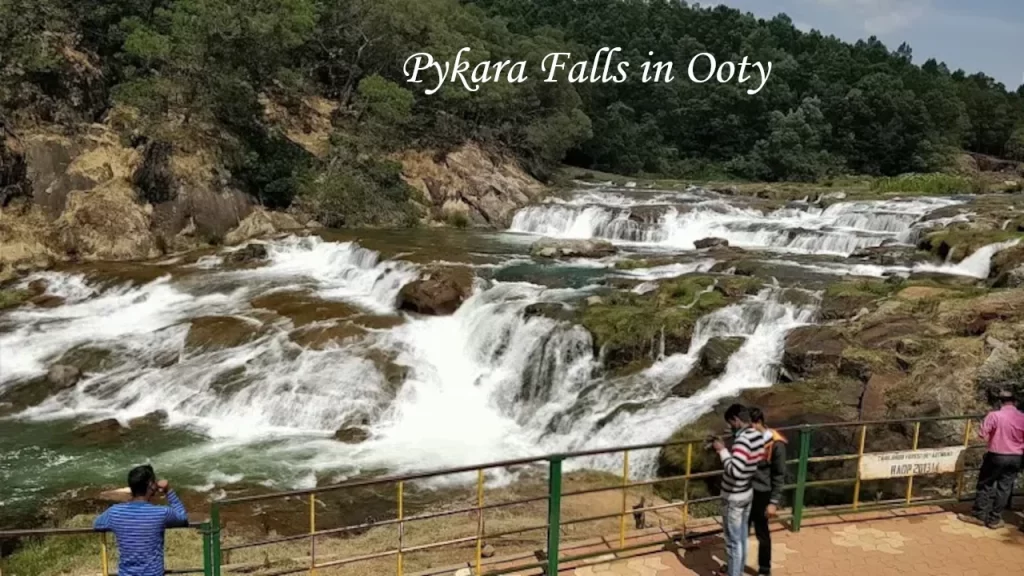 Scenic view of Pykara Falls cascading over rocks with tourists viewing from a fenced platform in Ooty.
