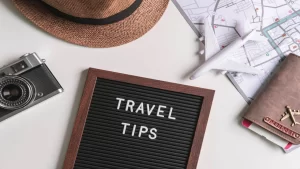 Flat lay of a camera, straw hat, passport, map, toy plane, and travel tips letterboard for trip planning inspiration.