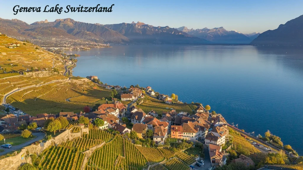 Panoramic view of Geneva Lake Switzerland with vineyards, lakeside village, and Alpine mountains under a clear blue sky