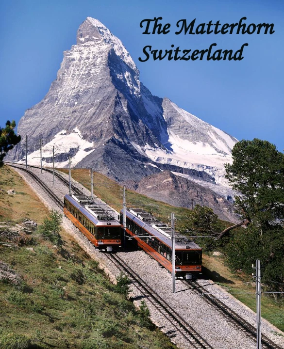 Two red cogwheel trains on parallel mountain railway tracks with the iconic pyramid-shaped Matterhorn peak rising behind green alpine slopes under a clear blue sky, Switzerland.