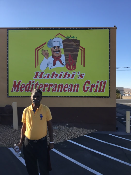 Visitor standing in front of Habibi’s Mediterranean Grill restaurant sign featuring Mediterranean cuisine branding and outdoor restaurant entrance
