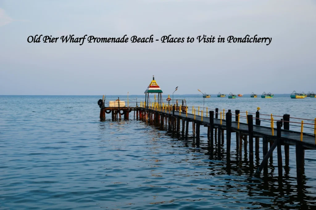 An old wooden pier and wharf stretching into the blue ocean with fishing boats in the background, a scenic highlight among places to visit in Pondicherry.